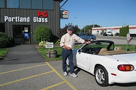 A person standing next to a white convertible in front of a Portland Glass location.
