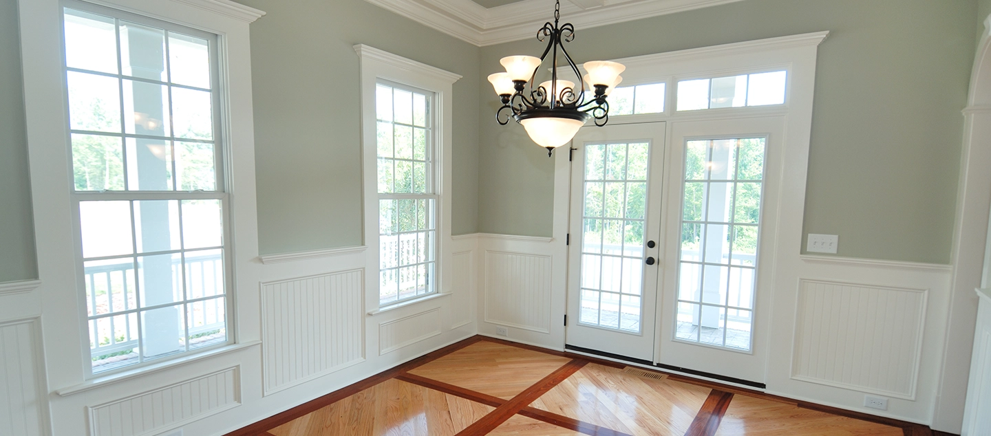 An empty room naturally lit by large glass windows and doors.