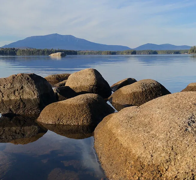 View Of A Beautiful Lake With Rocks And A Mountain.